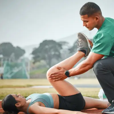 Physiotherapist helping woman with leg stretch exercise outdoors