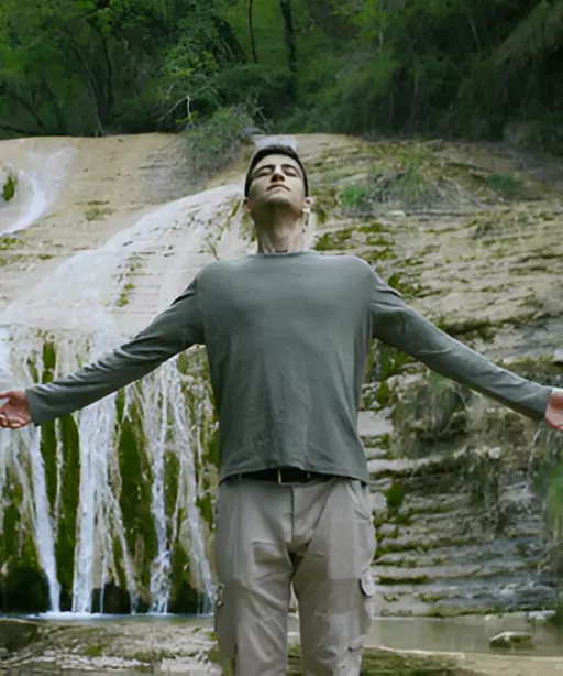 Man standing outdoors with arms open practicing deep breathing near waterfall